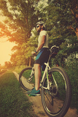 male athlete standing on a dirt road with a bicycle in the park in the spring