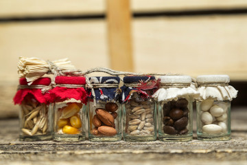 Small jars with uncooked grains , coffee beans and seeds on wooden background.