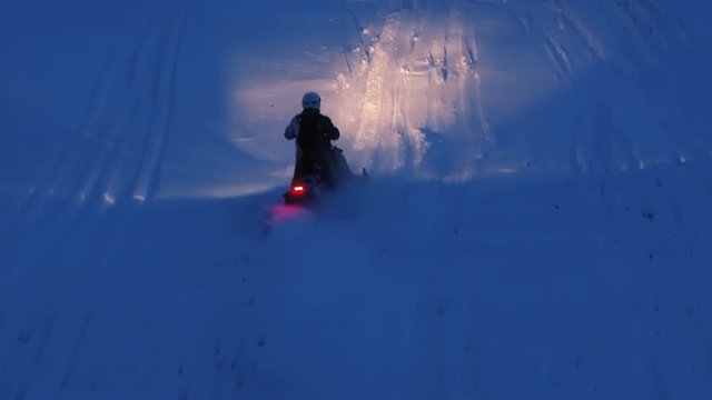 Aerial. A snowmobile is jumping through the snow at night