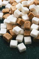A pile of scattered assorted sugar cubes on a dark background. Side view.
