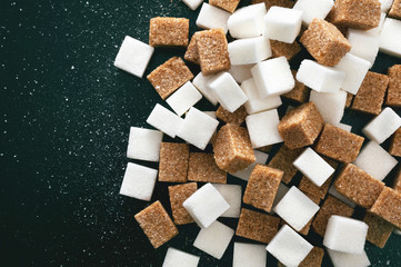 A pile of scattered assorted sugar cubes on a dark background. View from above.