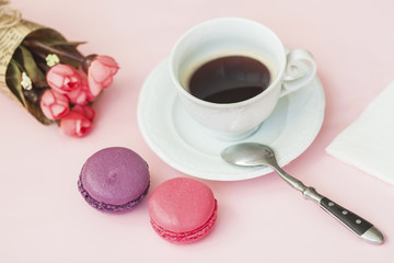 Pink and vioet macarons, macaroons, bouquet of spring flowers and cup of coffee, spoon, top view. Romantic morning, gift for beloved