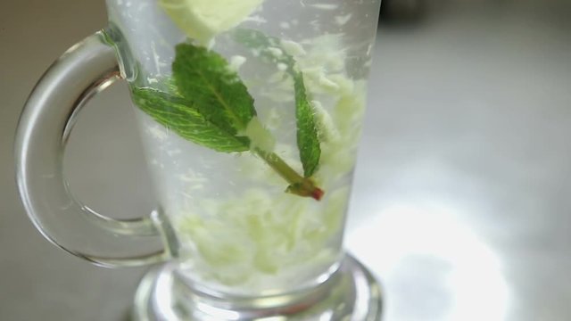 spoon stirring his tea with mint and lemon in a transparent glass, shot close-up