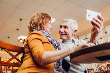 Senior couple makes a selfie using a phone in the cafe. Celebrating anniversary.