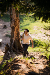 Happy bearded man traveler with backpack walking in forest. Tourism, travel, adventure, hike concept - smiling young man walking with backpack in woods. Concept of clean air and healthy lifestyle.