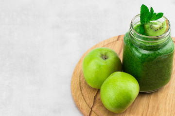 Healthy green smoothie with spinach in a jar mug with ingredients on wooden background with copy space