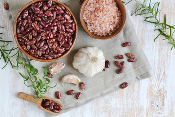 Raw red kidney beans in wooden bowl, rosemary herb, garlic, sea salt, healthy vegetarian food, lunch