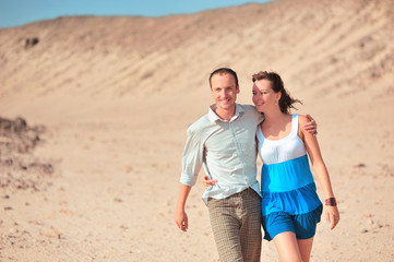 Fototapeta premium Happy young couple having fun in desert sand on vacation honeymoon travel holidays. Caucasian woman and man playing playful enjoying love on date. Multiracial couple