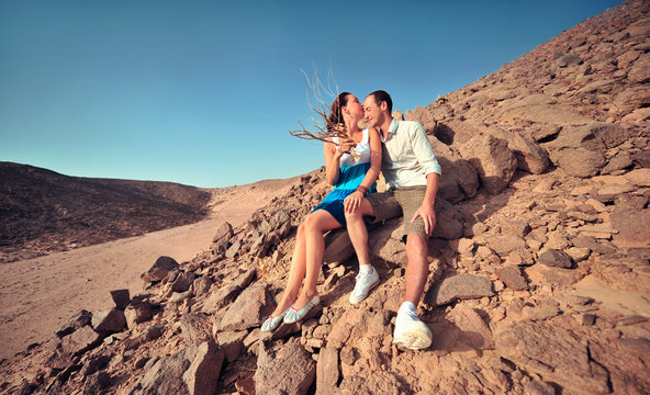 Happy young couple having fun in desert sand on vacation honeymoon travel holidays. Caucasian woman and man playing playful enjoying love on date. Multiracial couple
