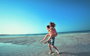 Happy young couple having beach fun on vacation honeymoon travel holidays. Caucasian woman and man...