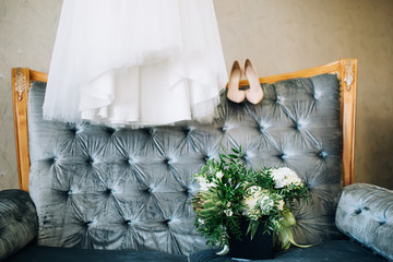 a wedding bouquet with a green panthea on a background of pink shoes and a wedding dress stands on a velvet blue sofa