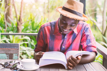 African american man reading a book with coffee , key ,smartphone and green natural background.