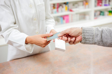 Medicine, pharmaceutics, health care and people concept - Senior customer and young pharmacist holding a credit card