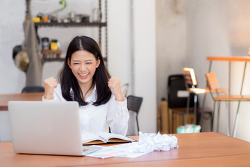 Beautiful asian young woman working online on laptop sitting at coffee shop, professional female freelancer with paper crumpled and using notebook computer with connect to internet for distance job.