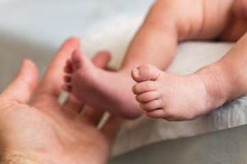 The hand of an adult touches the little leg of the infant
