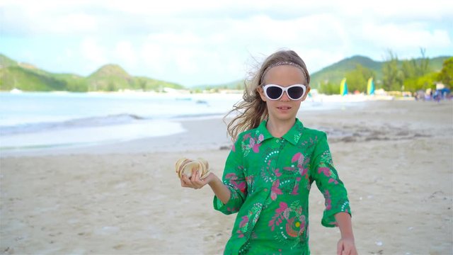 Little cute girl with seashell in hands at tropical beach. Adorable little girl playing with seashells on beach