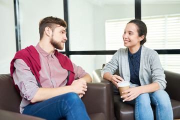 Attractive female manager sitting in chill-out zone, listening to handsome male colleague and smiling cheerfully