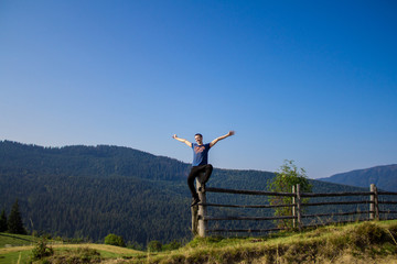 Man with hands up on top of mountains with blue sky. Man enjoying free happiness in beautiful landscape. Travel concept
