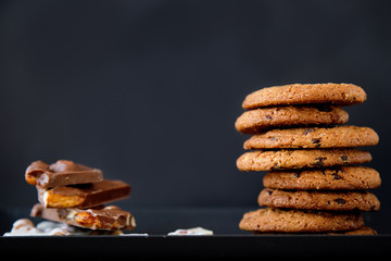 close-up of pieces of white and black chocolate with nuts and cookies on a black plate on a black...