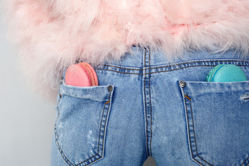 close-up of pink and minty macaroons that lie in the pockets of the girl's jeans in a pink fur coat turned back