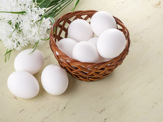 Fresh eggs in a basket and on a wooden table. Against the background of white flowers