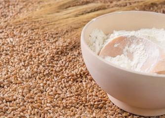 Flour in a wooden bowl, wheat against a background of wheat grains.