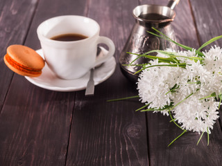 Cup of coffee, macaroni on a plate and a bouquet of flowers.