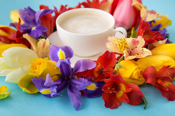 Obraz na płótnie Canvas A white forfor-cup with a saucer and coffee around which lie tulips, nartsisov, and orchad who lie on a blue background