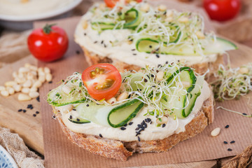 Healthy vegetarian bruschettas with bread, micro greens, hummus, cherry tomatoes, cucumbers and pine nuts