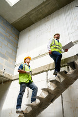Full length portrait of construction foreman and supervisor walking up stairs in unfinished building