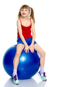 A little girl is jumping on the big gym ball.