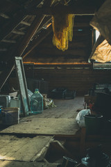 Old barn with a lot of stuff laying around. Sunlight from the window shines upon empty glass bottles. Wooden and aged interior.