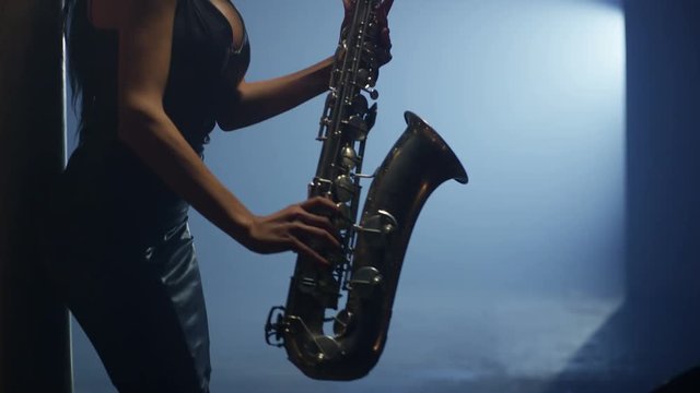 Young, beautiful, sexy, brunette woman dancing and playing golden saxophone on dark background . Shot on RED HELIUM Cinema Camera in slow motion. 