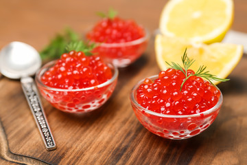 Bowls with delicious red caviar on wooden board, closeup