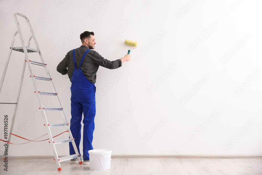 Poster young male decorator painting wall in empty room