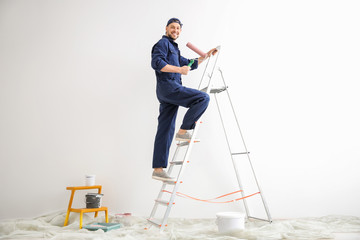 Young male decorator with paint roller in empty room