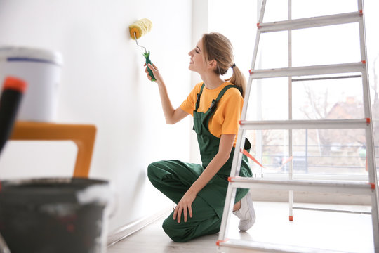 Young female decorator painting wall in room