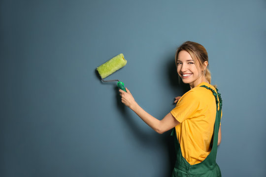 Young female decorator with paint roller near color wall