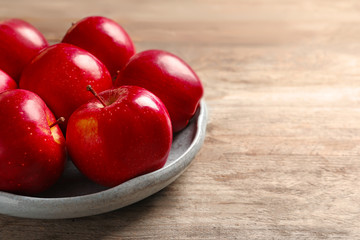 Plate with ripe red apples on wooden background