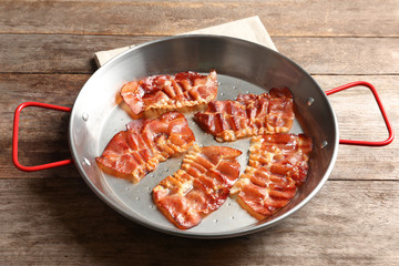 Dish with fried bacon on wooden background