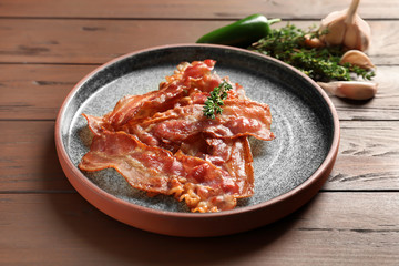 Plate with fried bacon on wooden background
