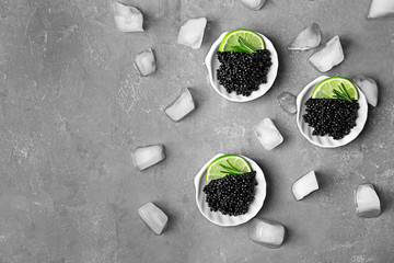 Plates with black caviar and ice cubes on grey background