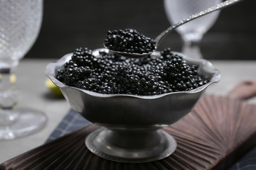 Metal bowl with black caviar on wooden board