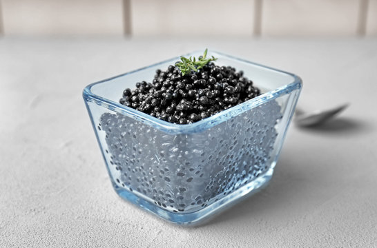 Glass bowl with black caviar on grey background