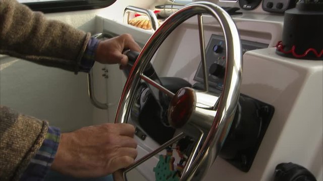 Older mans hand on the steering wheel and throttle stick of a boat.