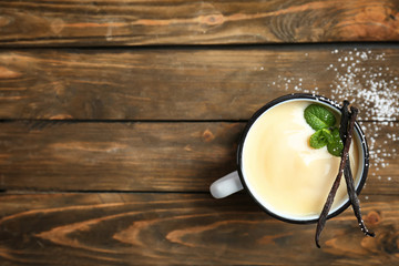 Mug with vanilla pudding, sticks and fresh mint on wooden background