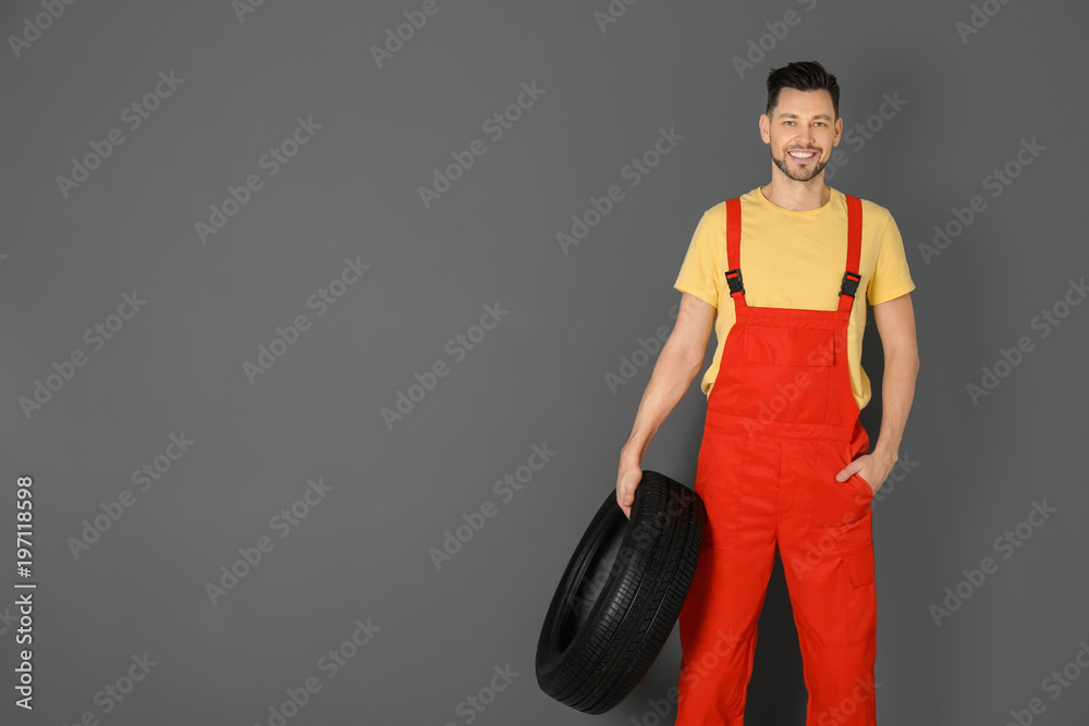 Wall mural Male mechanic with car tire on color background