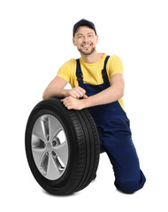 Male mechanic with car tire on white background