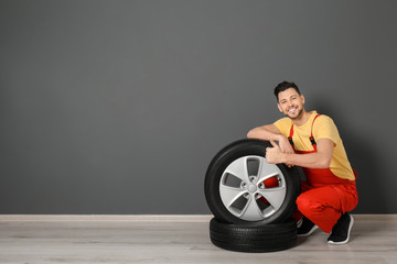 Fototapeta na wymiar Male mechanic with car tires on color wall background
