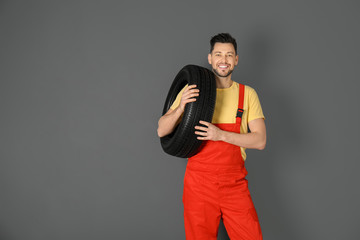 Male mechanic with car tire on color background